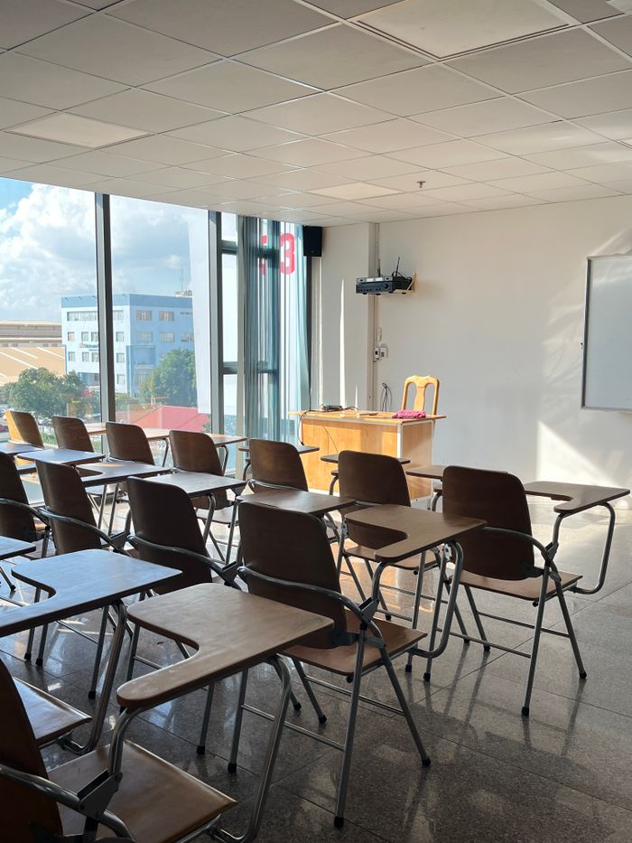 Bright, sunlit classroom with wooden desks and large windows offering a city view.