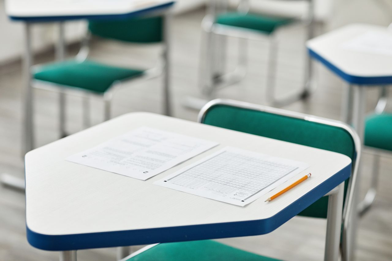 About A close-up of an empty classroom desk with exam papers and a pencil, highlighting education and testing environment.